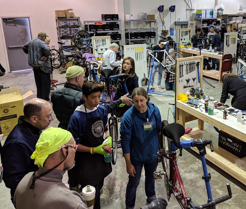 Many volunteers repairing bicycles at workbenches in a large bicycle repair workshop