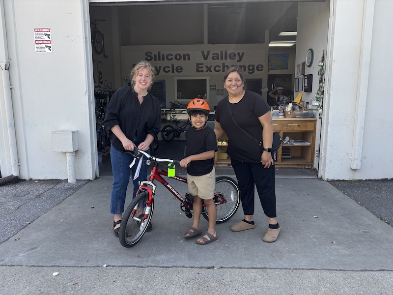 Two adults and a boy holding a bike, in front of the Bicycle Exchange shop