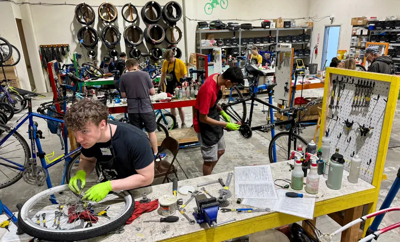 Several volunteers repairing bicycles at workbenches in a well-furnished shop